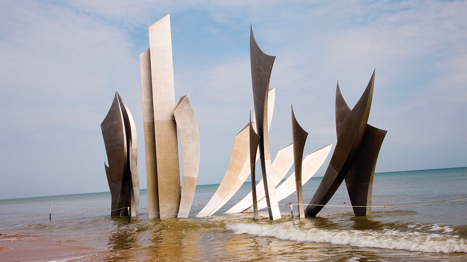 On Omaha Beach’s shore, waves come upon Les Braves, a monument commemorating Allied troops who landed on June 6, 1944.