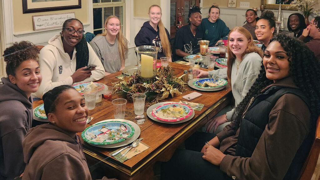 NC State women's basketball players sit around a holiday dinner table.