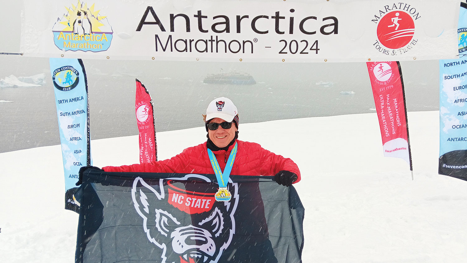 Bryan Benton holds up a Wolfpack flag after completing the 2024 Antarctica Marathon.