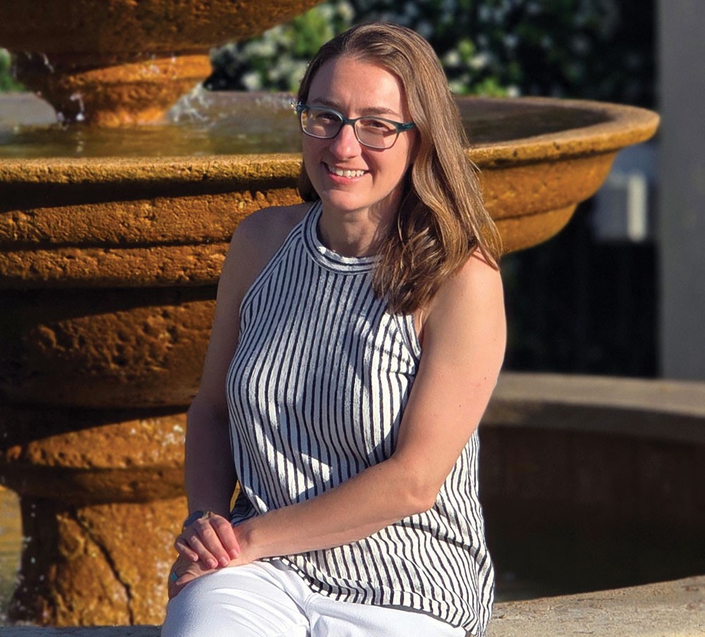 A portrait of Jessica Berrett sitting on the edge of a decorative water fountain.