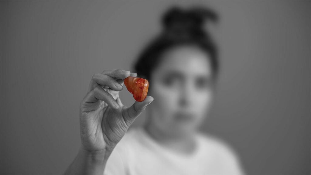 A black-and-white photograph of a blurred woman in the background holding up an amber stone. The focus is on the stone.