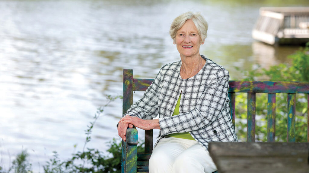 A portrait of Sara Rajala sitting on a bench at the edge of Lake Raleigh.