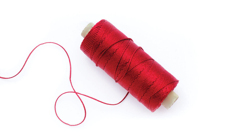 A spool of red thread with loose strands against a white background.