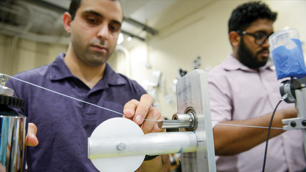 Two textile students work with medical suture fiber on laboratory equipment.