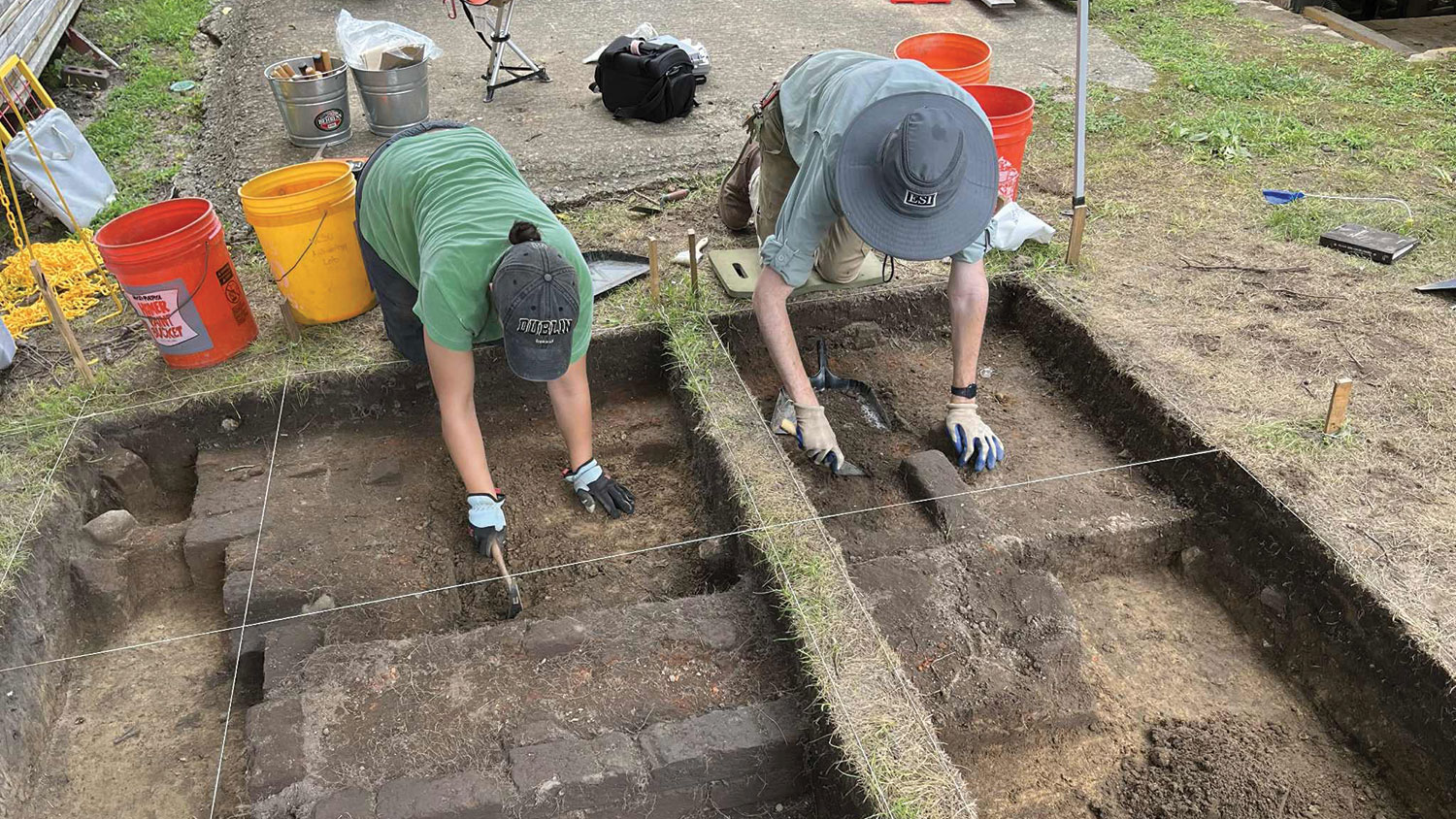Archaeology students dig in the ground with spades.